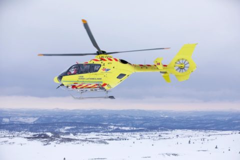 Gelber Rettungshubschrauber fliegt über verschneiter Landschaft.