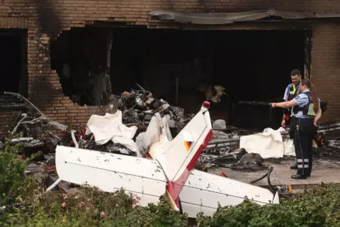 Polizisten schauen sich die Reste eines abgestürzten Flugzeugs an auf der Terrasse eines Wohnhauses.